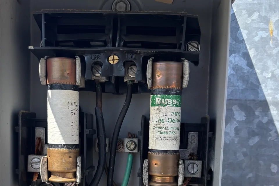 Alpha Mechanical service photo: an open fused AC disconnect with the plastic around the fuse holder and line terminals melted and blackened after loose connections overheated under overcurrent