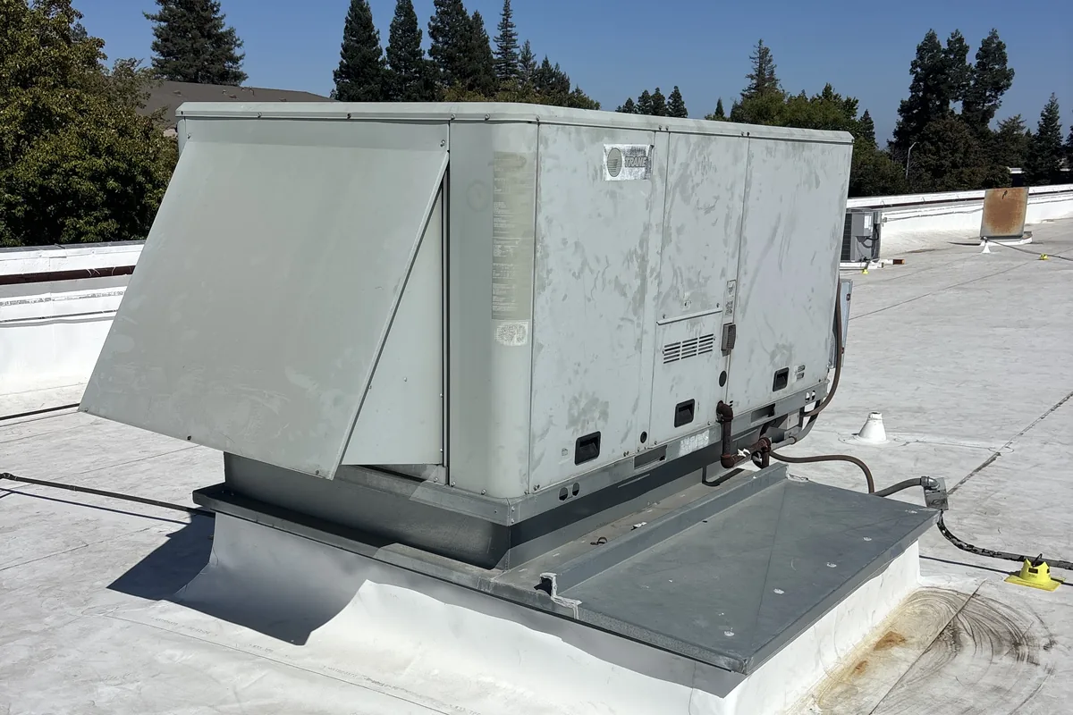 Trane light commercial rooftop package unit on its curb, service panel open, on a flat Sacramento-area roof