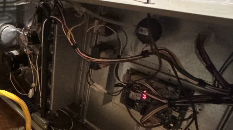 Inside the same attic furnace cabinet on an Alpha Mechanical call: the control board with its status light lit, the wiring harness and the inducer motor, the parts inspected for an electrical burning smell