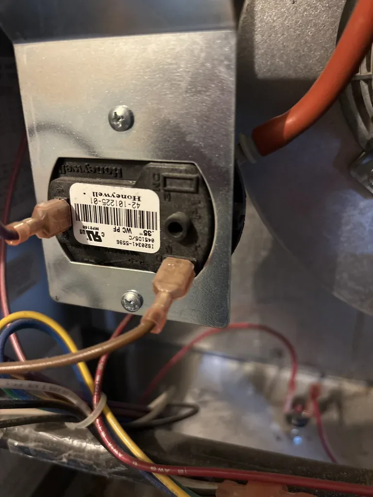 A Honeywell furnace pressure switch on its mounting bracket beside the inducer, wired with two spade terminals, photographed on our February 2026 call in Fair Oaks 95628
