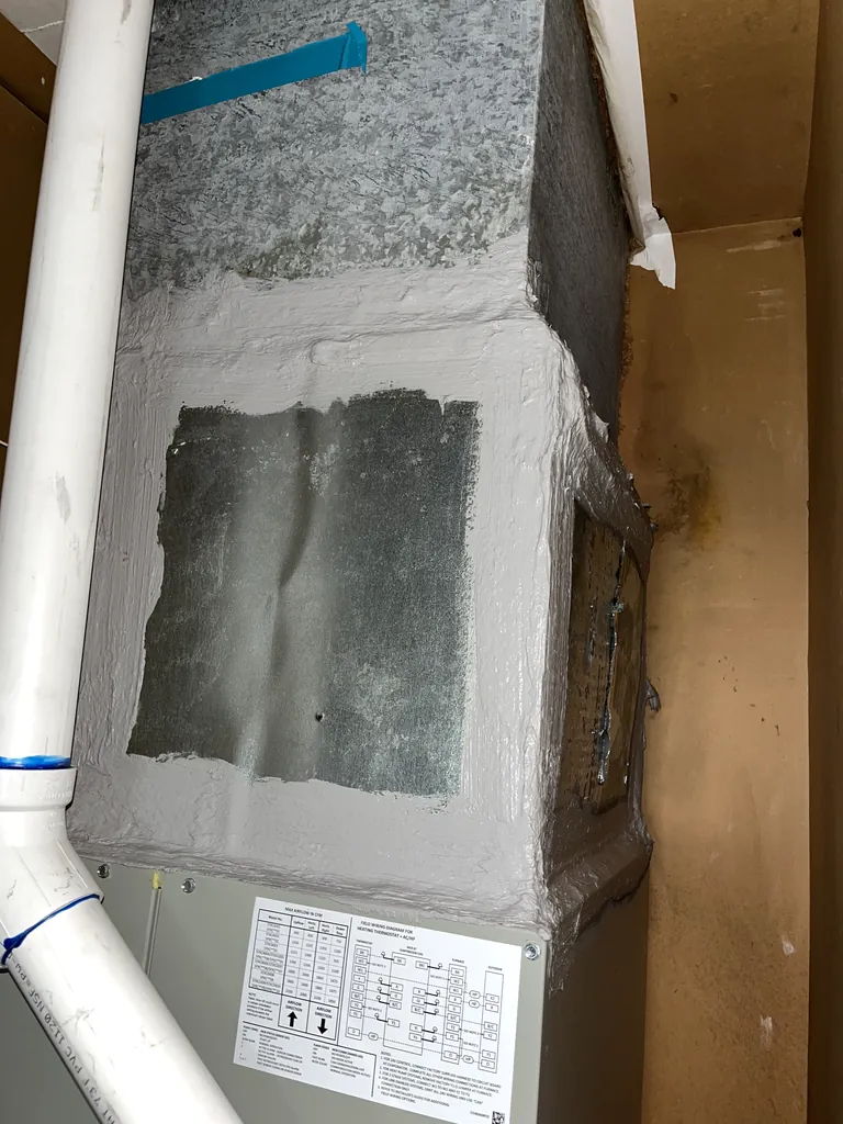 Gray mastic sealing the seams where the supply plenum meets the new equipment on a Carmichael furnace and AC replacement in February 2026