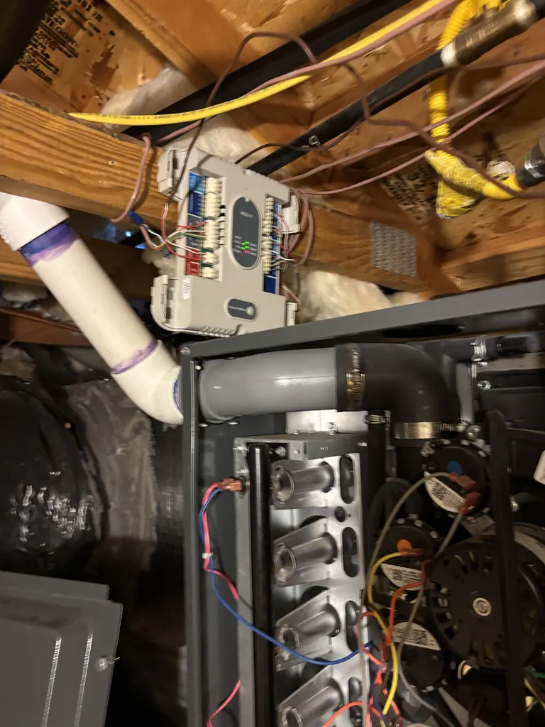 An attic high-efficiency gas furnace in Sacramento with its burner compartment open on an Alpha Mechanical service call in September 2026, showing the row of burners, the wiring, and the plastic vent pipe joining the furnace through a rubber coupling