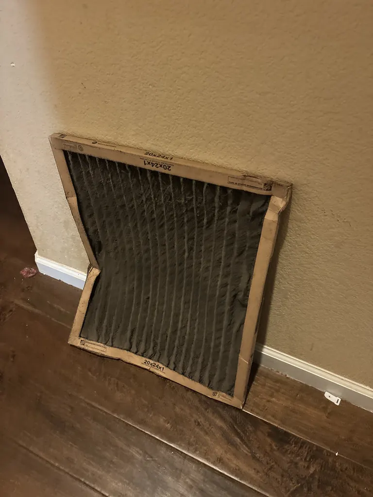 A heavily loaded 20x24x1 pleated air filter, its media bowed out of the frame, pulled from a return grille in a Sacramento home on an Alpha Mechanical service call in July 2026