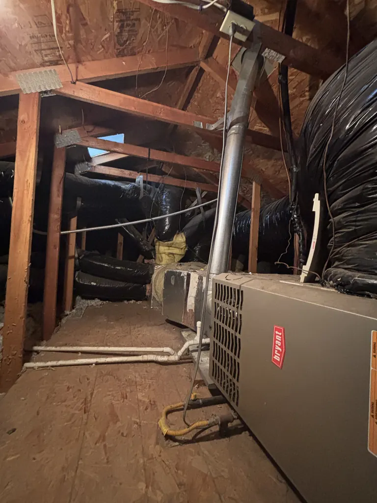The single-stage Bryant gas furnace this West Sacramento home replaced, lying horizontally in the attic with its metal flue pipe rising to the roof, photographed at the estimate visit in March 2026
