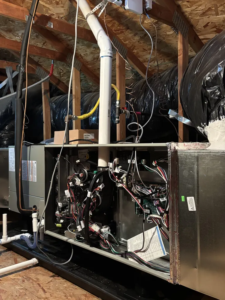 A new Trane two-stage condensing gas furnace installed horizontally in a West Sacramento attic in spring 2026, front panel off during the install, with its white PVC vent pipe rising to the roof and PVC condensate drain lines leaving the cabinet
