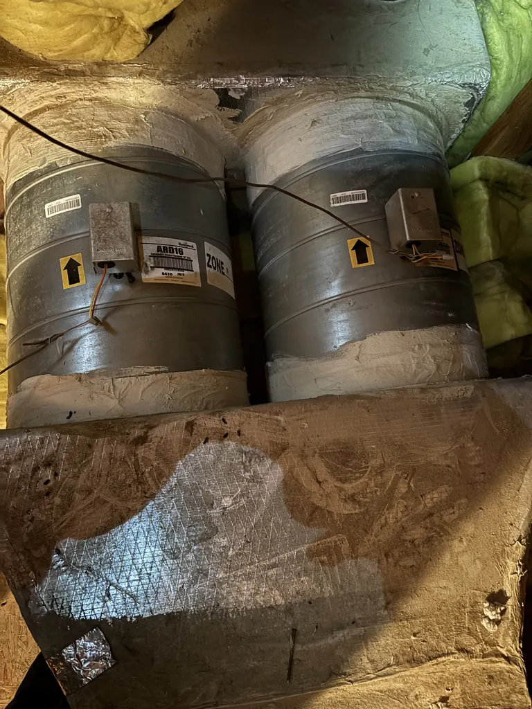 Two 16-inch Honeywell zone dampers side by side on the supply ducts in the West Sacramento attic, each with its damper motor wired, photographed on the spring 2026 furnace replacement job