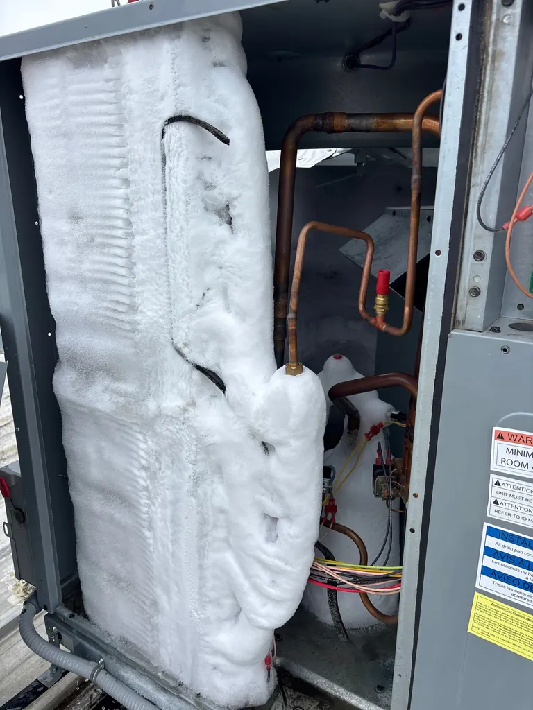 Outdoor coil buried under solid ice behind the open access panel of a heat pump, copper refrigerant lines frozen over