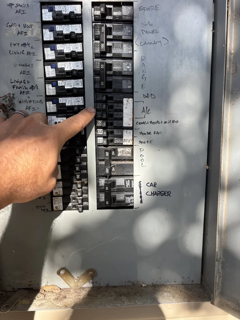 A labelled home breaker panel on an Alpha Mechanical service call in Sacramento in July 2026, with the technician pointing at the breaker marked A/C
