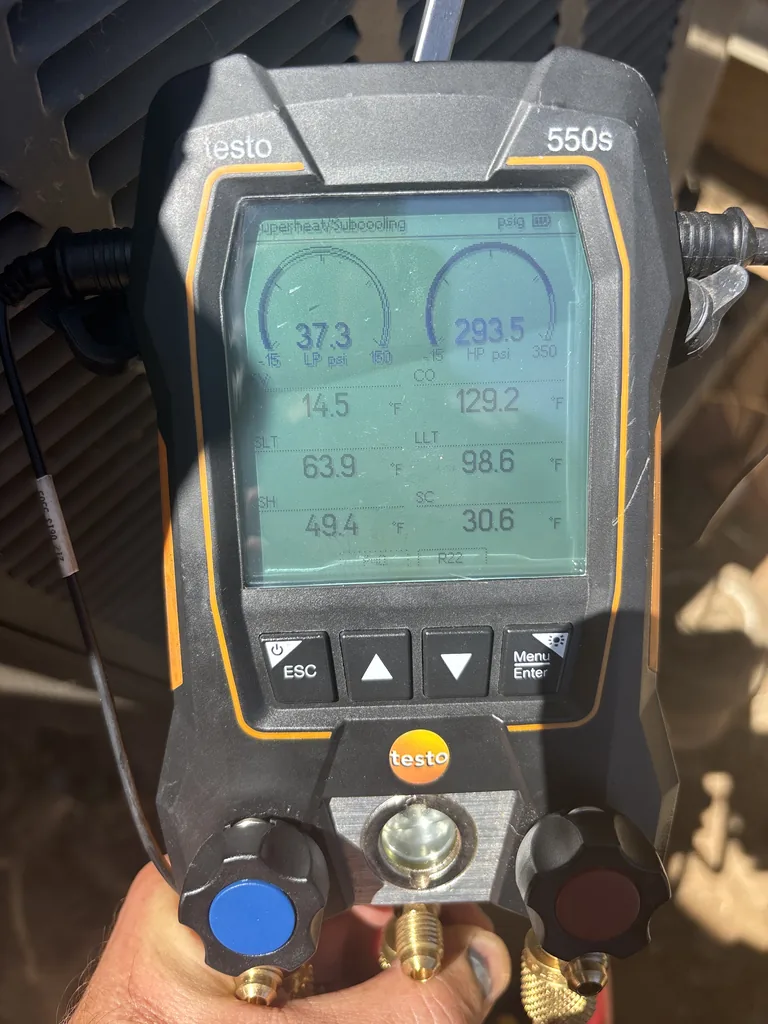 A Testo 550s digital manifold connected to a running air conditioner at the condenser, screen showing high-side and low-side pressures with superheat and subcooling calculated