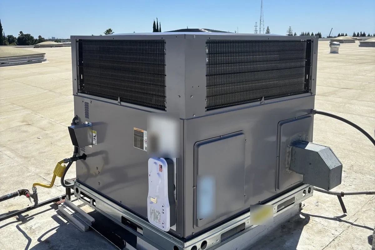A gray rooftop package unit on a flat Sacramento commercial roof, with its gas line, electrical disconnect and combustion vent hood on the side of the cabinet