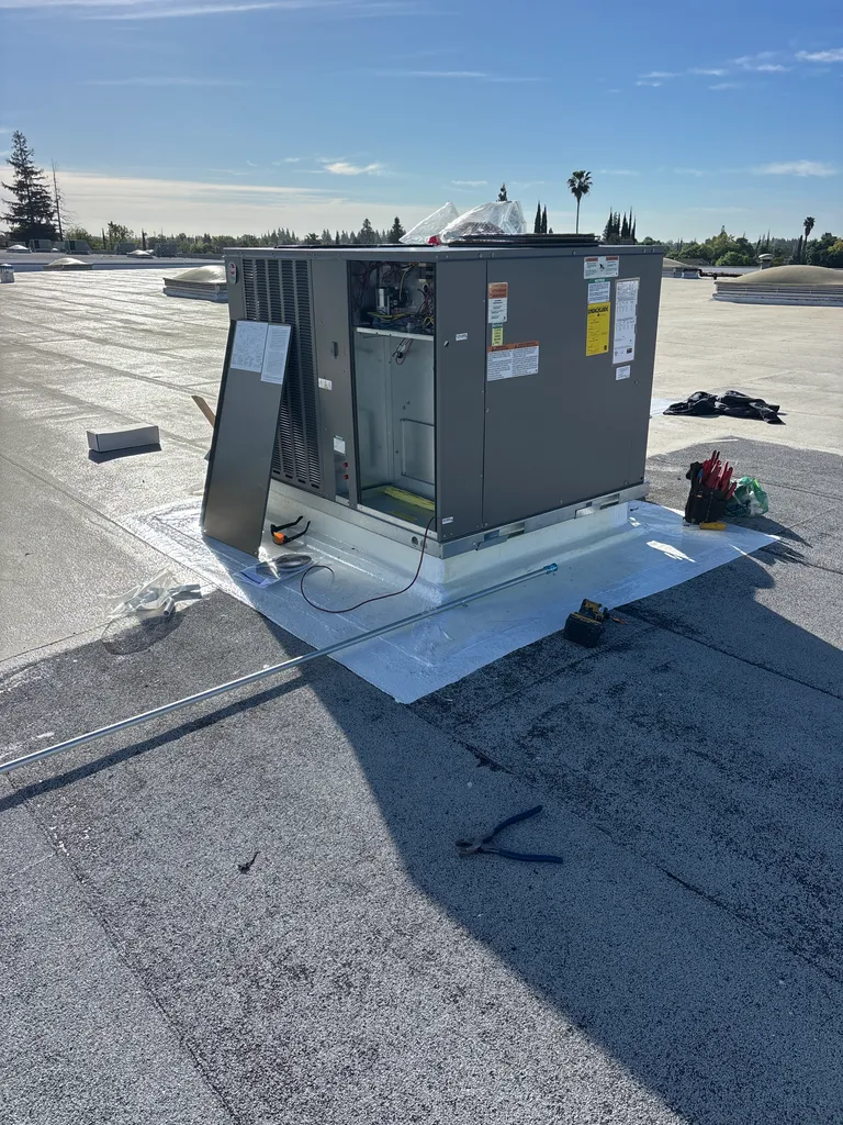 A new rooftop package heat pump Alpha Mechanical installed in 2026 on a commercial building in Sacramento, set on a new curb with fresh white roof flashing, its service panel off during installation