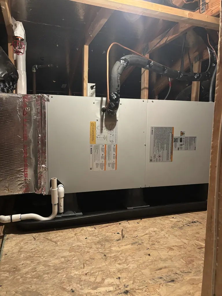 After: the new Bosch heat pump air handler lying horizontally in a Fair Oaks attic in July 2026, with insulated refrigerant lines entering its end, white condensate piping below, and the foil-wrapped plenum joining the existing ducts