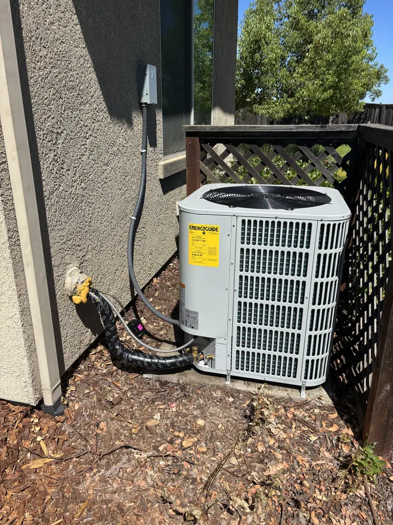After: the new Bosch heat pump outdoor unit on its pad beside a Fair Oaks house in July 2026, with a new electrical disconnect on the wall and insulated refrigerant lines entering the stucco