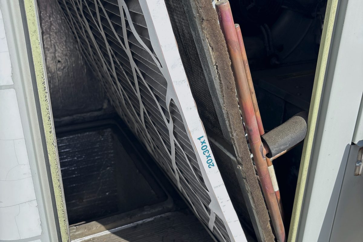 Technician pulling a 20x30x1 air filter from an HVAC unit during a maintenance tune-up